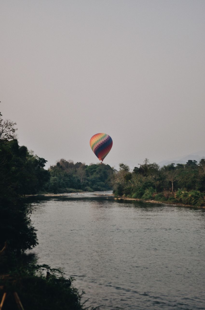 water, sky, adventure, transportation, flying, nature, mid-air, hot air balloon, tree, air vehicle, plant, day, beauty in nature, scenics - nature, extreme sports, parachute, balloon, lake, copy space, outdoors, freedom