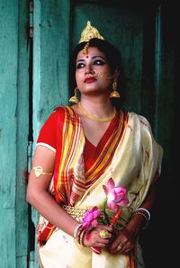 Bride in traditional clothing and topor standing against door