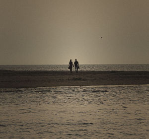 Silhouette people at beach against sky during sunset