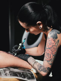 Young woman tattooing statue of liberty man on calf at parlor