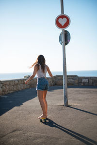 Full length rear view of woman walking on road against sky