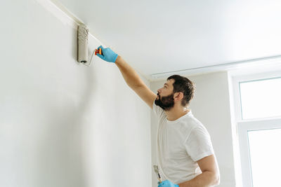 Caucasian bearded man painting wall with paint roller. painting apartment, renovating home