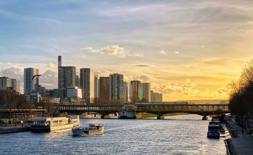 Bridge over river by buildings against sky during sunset