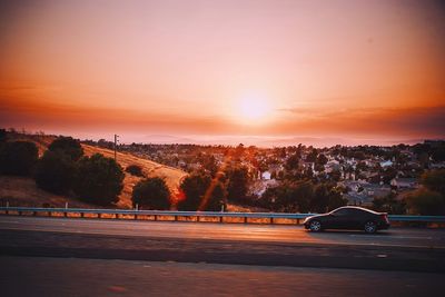 Road by trees against sky during sunset