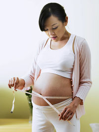 Pregnant woman measuring belly with tape measure