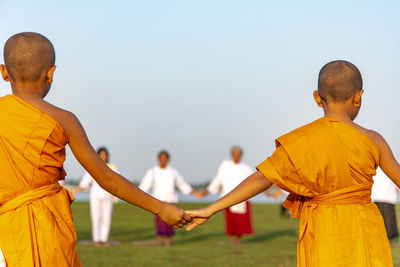 People holding hands while standing on land against clear sky