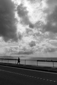 Man walking on road by sea against sky