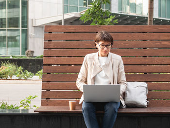 Freelance business woman sits in park with laptop and take away coffee. working remotely.