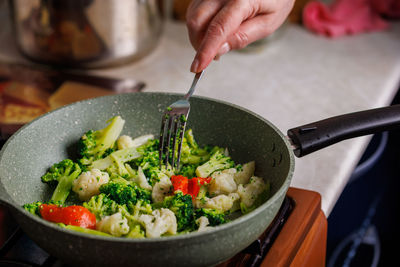 Caucasian senior woman hand with fork picks frying vegetables in frying pan