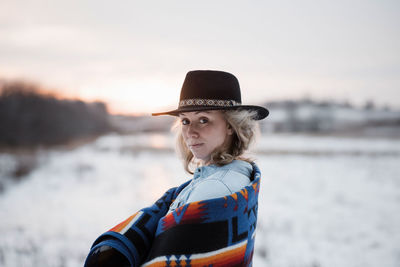 Portrait of woman standing in a field at sunset with hat and blanket
