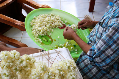 Midsection of woman making floral garland at home