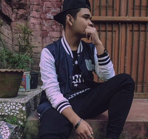 Young man looking away while sitting on wall