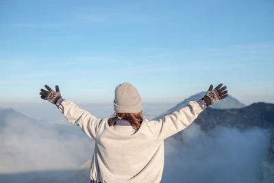 Rear view of woman with arms outstretched standing against sky