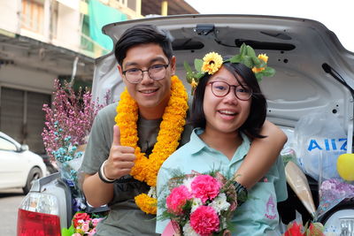 Portrait of smiling young couple holding bouquet at car trunk