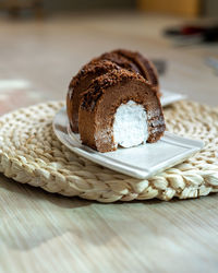 Chocolate roll with fresh cream on a white plate and wooden background