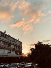 Cars on street by buildings against sky during sunset