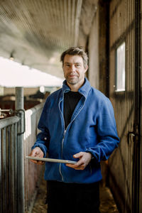 Smiling farmer with digital tablet standing at cattle farm