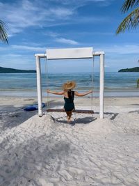 Rear view of woman looking at beach on swing