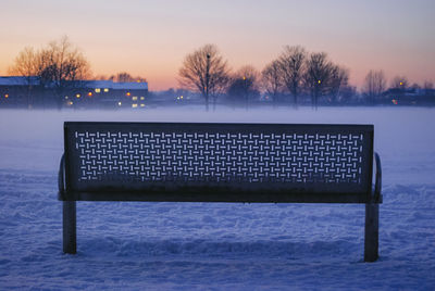 Bench by bare tree against sky during sunset