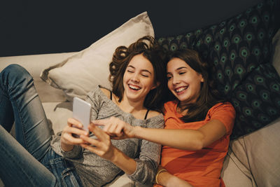 High angle view of happy friends using phone while resting on sofa at home