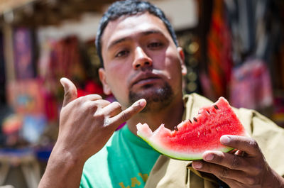 Portrait of man holding watermelon and gesturing while standing outdoors