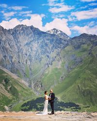 Bride and groom standing on mountain against sky