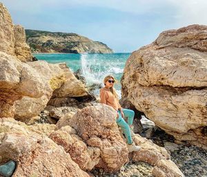 Woman on rock at beach against sky