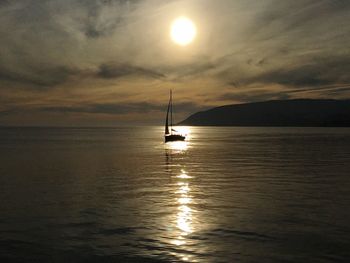 Silhouette sailboat in sea against sky during sunset