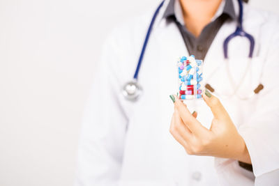 Midsection of female doctor holding pills against white background