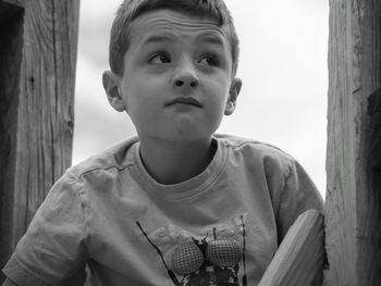 Close-up of boy making face by wooden post