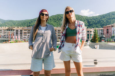 Two young cheerful girlfriends are talking and laughing on a summer morning in a skatepark