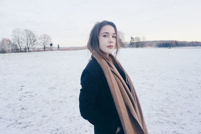 Portrait of beautiful woman standing on snow covered landscape against sky