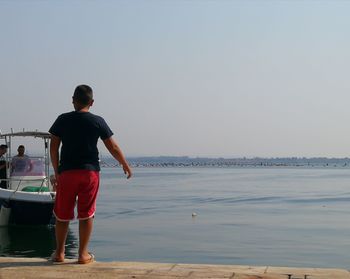 Rear view of man standing on sea against clear sky