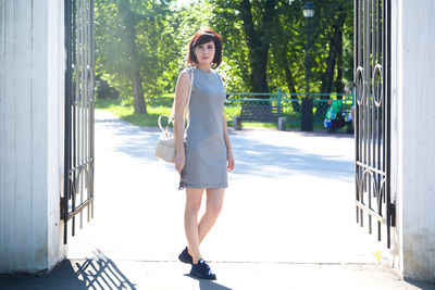 A woman in a short striped dress stands at the open gates of the park.