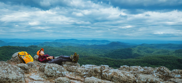 Rear view of woman sitting on rock against sky