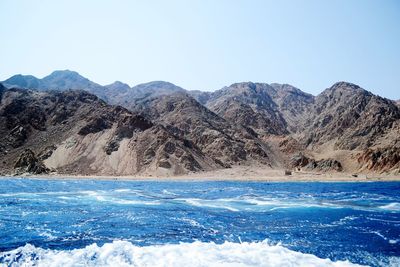 Scenic view of sea and mountains against clear blue sky