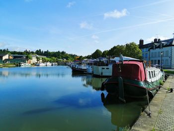 Boats moored on river by buildings against sky