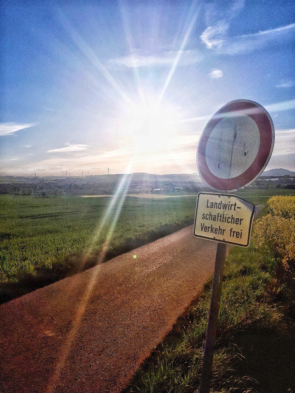 ROAD SIGN ON FIELD AGAINST BRIGHT SUN