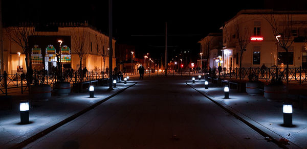 Illuminated street amidst buildings in city at night