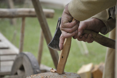 Midsection of carpenter cutting wood on tree stump