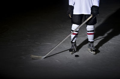 Low section of man playing ice hockey against black background