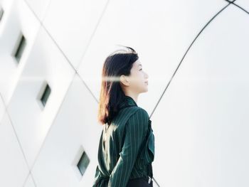 Side view of young woman looking away while standing by building