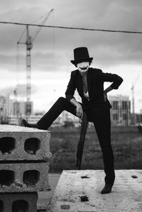 Full length of woman standing against sky in hat  and mask with gun