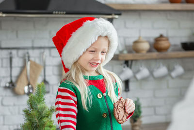 Girl in santa claus hat smiling and eating christmas cookie