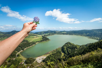 Cropped hand of woman holding flower against lake