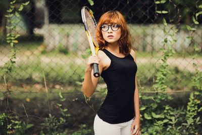 Portrait of young woman standing against chainlink fence