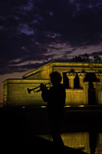 Silhouette man playing trumpet against temple of debod at night