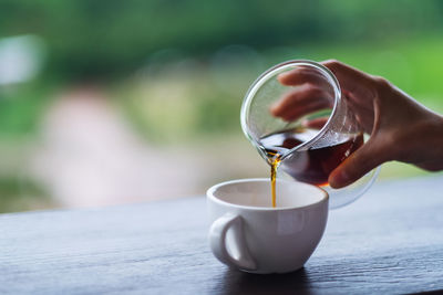 Closeup image of a hand pouring drip coffee into a white mug with blurred nature background