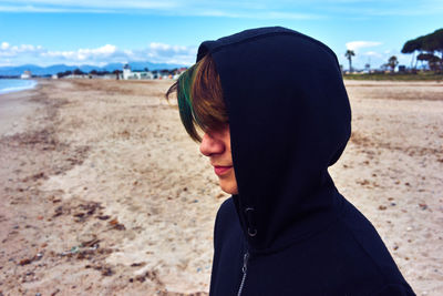 Rear view of boy on sand at beach against sky