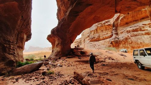 Rear view of man walking b y car on rock formation